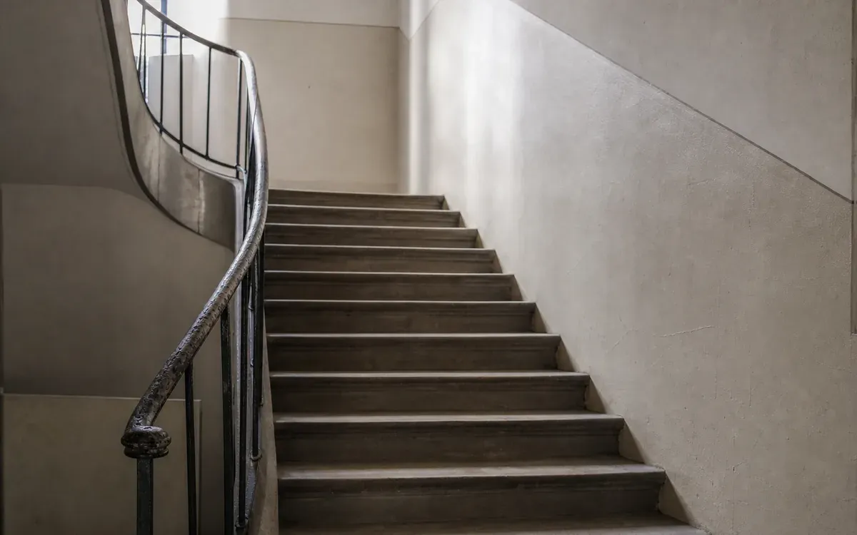 Escalier intérieur d'établissement scolaire avec rampe usée et lumière traversante
